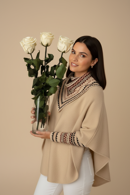 Model wearing beige Ecuadorian poncho holding trio of cream preserved roses in glass vase